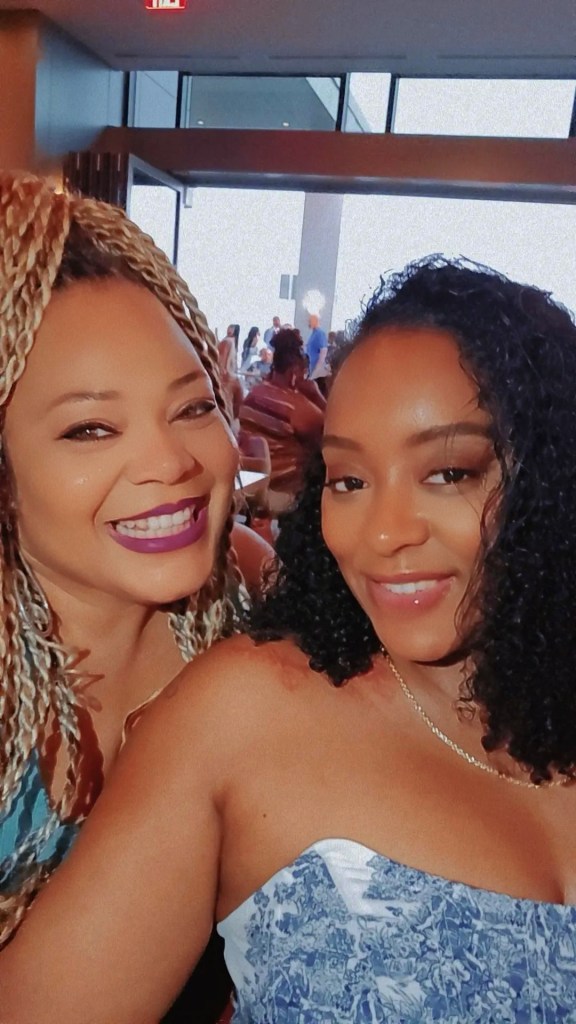 Two women smiling together in a vibrant, social setting, with a lively atmosphere in the background.